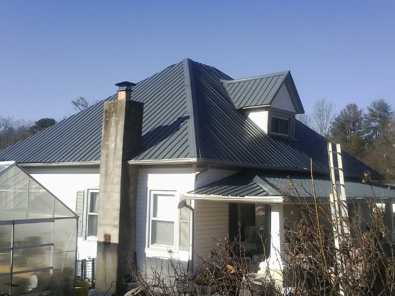 Dark blue standing seam metal roof on a white farmhouse with dormer — Slate & Tile Roof Repair by Roofing Brothers in Amanda
