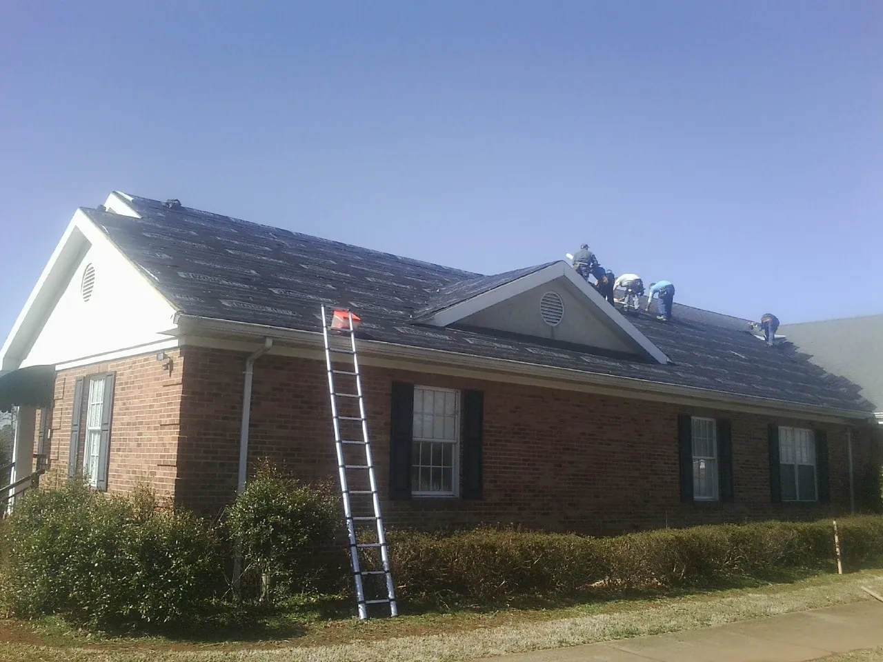 Crew tearing shingles off a brick ranch roof with a ladder set — Metal Roof Repair work by our crew in Amanda