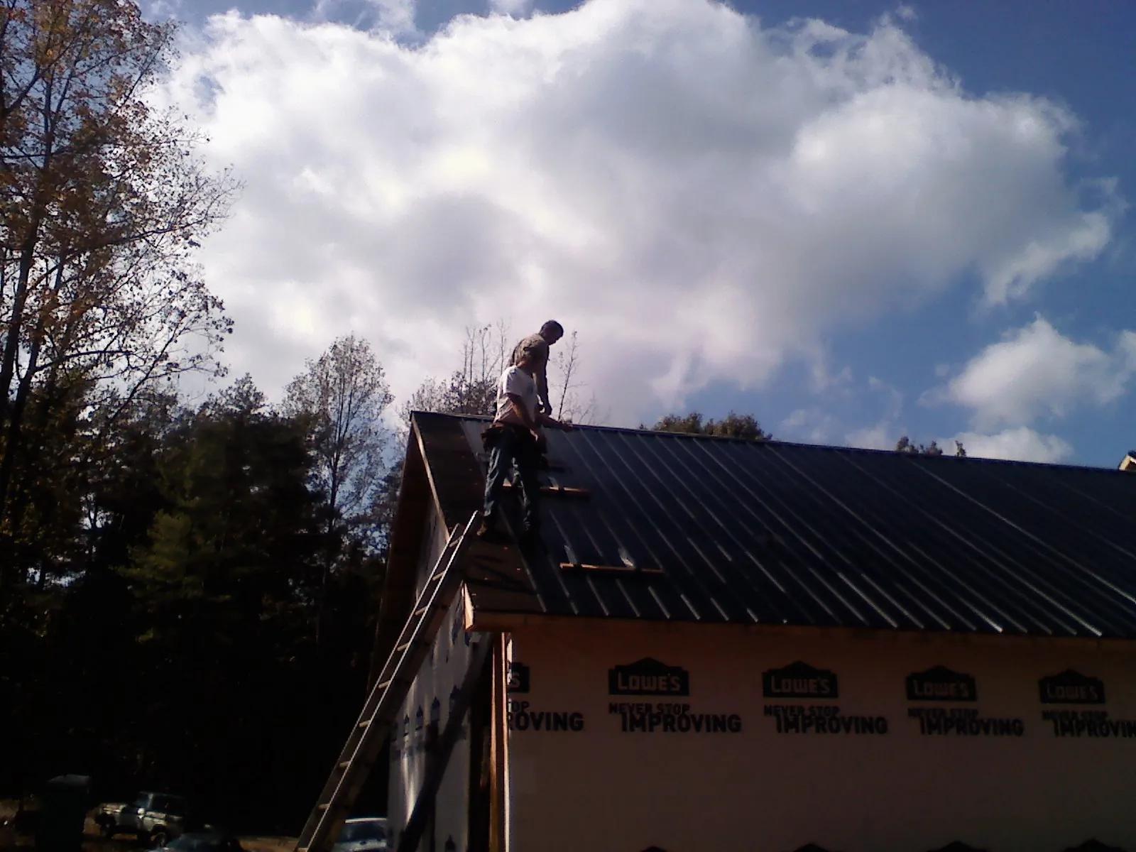Roofer fastening dark metal panels high against a cloudy sky, from a Roof Inspection job in Amanda